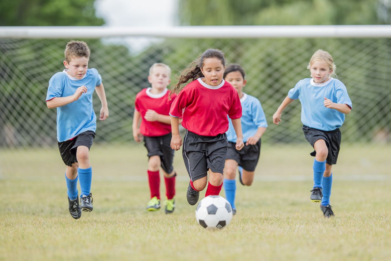 Children playing soccer chase a ball